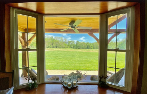 A view through a large window showcasing a green lawn and a covered patio with a ceiling fan.