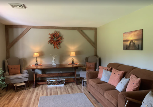 Cozy living room with a brown sofa, two armchairs, a wooden table, and warm lighting, featuring decorative wall art.