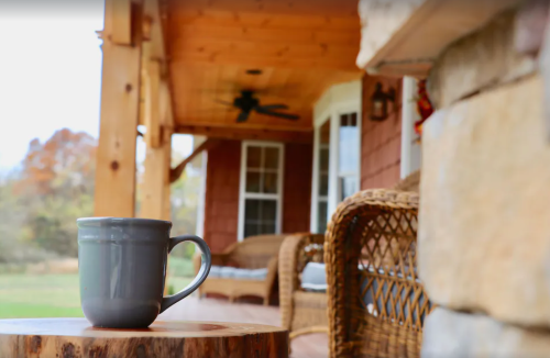 A cozy porch scene featuring a gray mug on a wooden table, with wicker chairs and a view of greenery in the background.