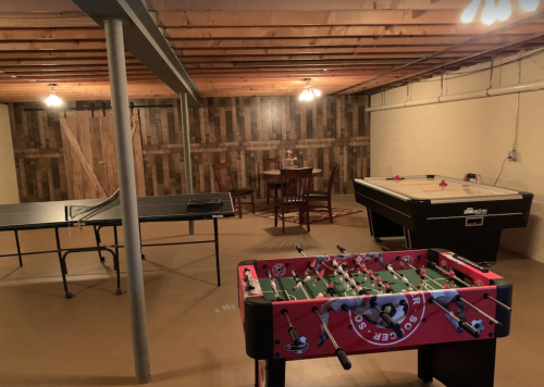 A basement game room featuring a foosball table, air hockey table, ping pong table, and a dining area.