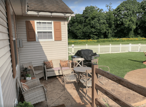 A patio area with outdoor furniture, a grill, and a view of a green lawn and trees in the background.