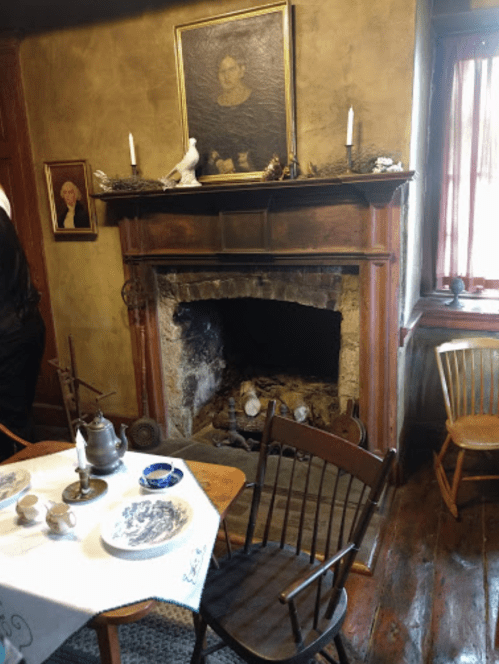 A cozy room with a fireplace, vintage furniture, and a table set for tea, featuring portraits on the walls.