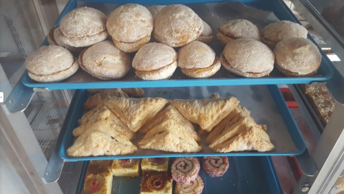 A display case with three shelves of assorted baked goods, including cookies, pastries, and sweet rolls.