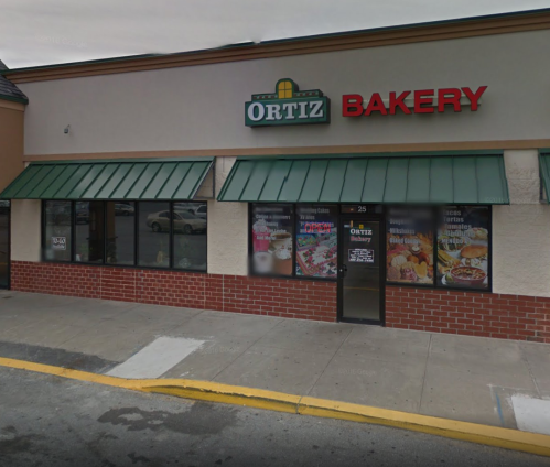Exterior of Ortiz Bakery, featuring a green awning and large signage, with display windows showcasing various baked goods.