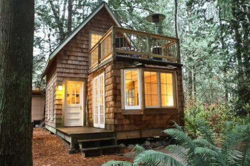 Cozy wooden cabin nestled in a forest, featuring a deck and warm lights glowing from the windows.