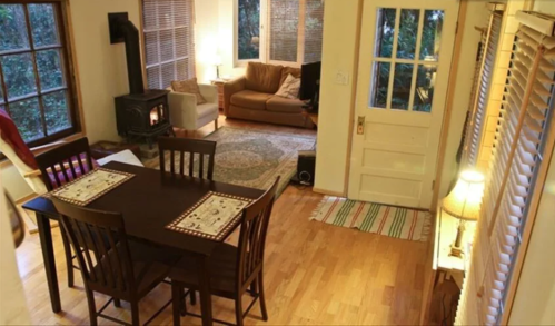 Cozy living space with a dining table, a sofa, a wood stove, and large windows letting in natural light.