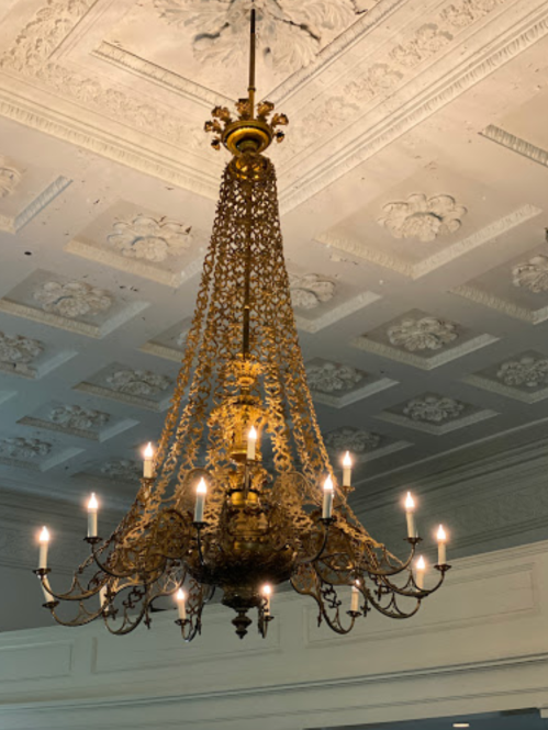 A grand, ornate chandelier with multiple candles hangs from a decorative ceiling.