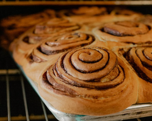 Freshly baked cinnamon rolls in a pan, with golden-brown swirls and a soft texture, cooling in an oven.