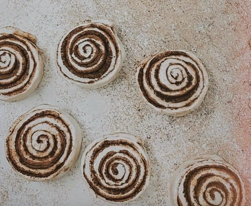 Six cinnamon roll dough pieces arranged on a light surface, showcasing their spiral patterns.