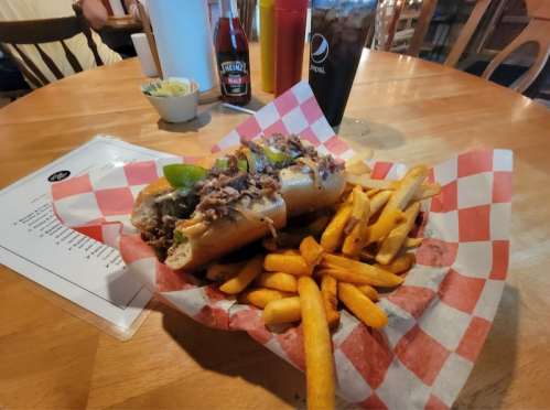 A plate of two loaded hot dogs topped with onions and peppers, served with a side of golden fries on a checkered paper.