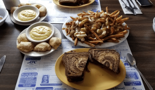 A table with a plate of poutine fries, two bowls of soup, and slices of marbled bread.