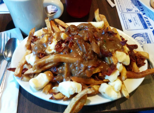 A plate of poutine topped with gravy, cheese curds, and crispy bacon, served with fries.