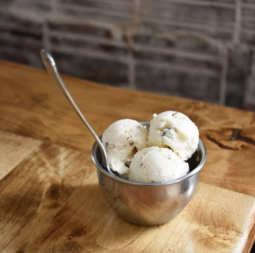 A metal bowl filled with three scoops of vanilla ice cream with chocolate chips, resting on a wooden table.