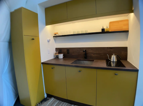 Modern kitchen with yellow cabinets, a dark countertop, a sink, and a kettle on the shelf.