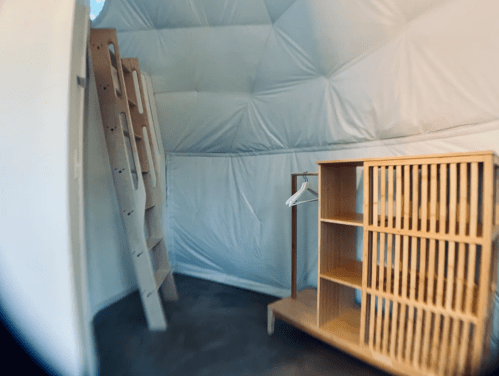 Interior of a dome-shaped room featuring a wooden ladder, shelving unit, and minimalist decor.
