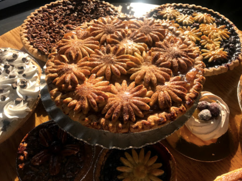 A variety of beautifully decorated pies with floral designs, displayed on a wooden surface, illuminated by natural light.