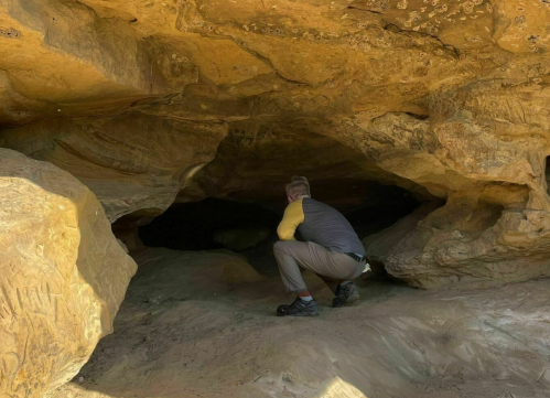 A person crouches inside a rocky cave, surrounded by textured stone walls and shadows.