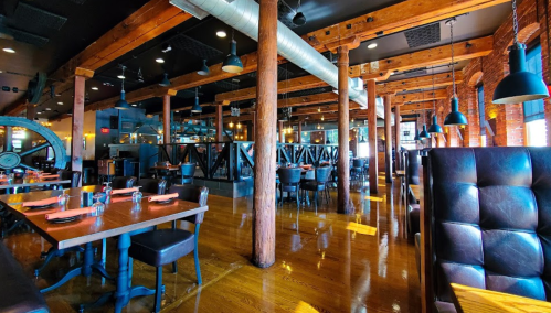 A spacious restaurant interior with wooden beams, tables set for dining, and warm lighting.