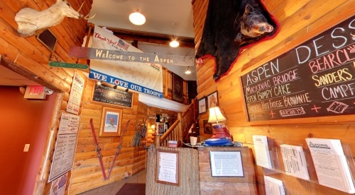 Cozy wooden interior of a lodge with a welcome sign, menu boards, and mounted animal heads on the walls.