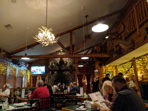 Cozy restaurant interior with wooden beams, warm lighting, and diners enjoying meals at tables.