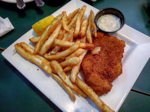 A plate of golden French fries, a crispy fried fish fillet, a lemon wedge, and a small cup of dipping sauce.
