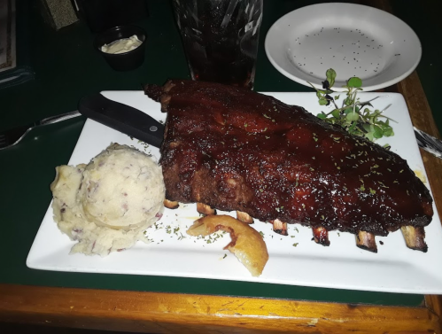 A plate featuring a large rack of ribs glazed with sauce, served with mashed potatoes and a side of greens.