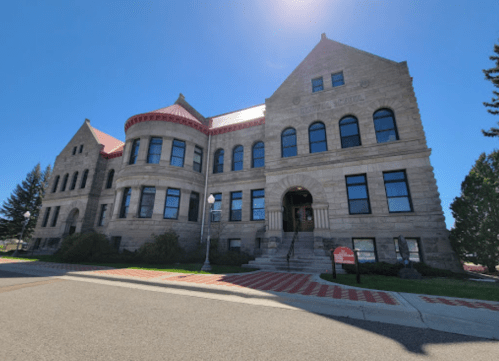 Historic stone building with a red roof, large windows, and a staircase, set against a clear blue sky.