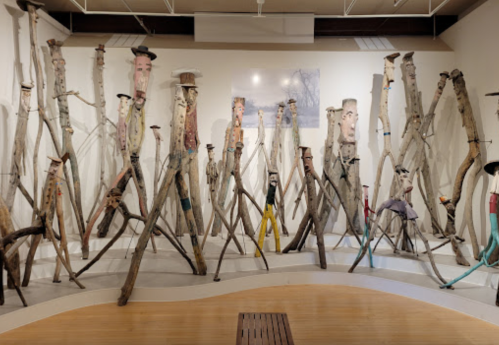 A gallery filled with tall, painted wooden figures resembling people, arranged in a creative display.