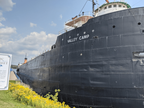 A large black ship named "Valley Camp" docked near a grassy area with a sign in the foreground.