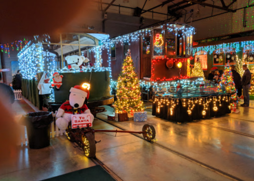 A festive display featuring a decorated train, Christmas tree, and a large Snoopy in a Santa hat.