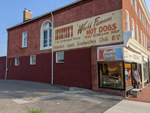 A vintage brick building with a sign for "Skeeter's World Famous Hot Dogs" and a storefront displaying Pepsi products.