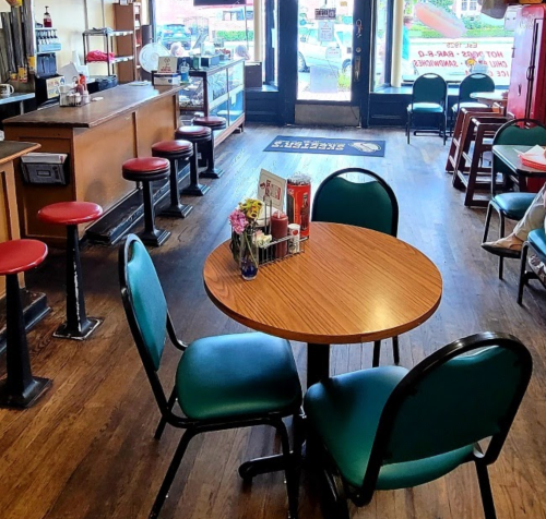 A cozy diner interior with a round table, four chairs, and a counter, featuring red stools and a welcoming atmosphere.