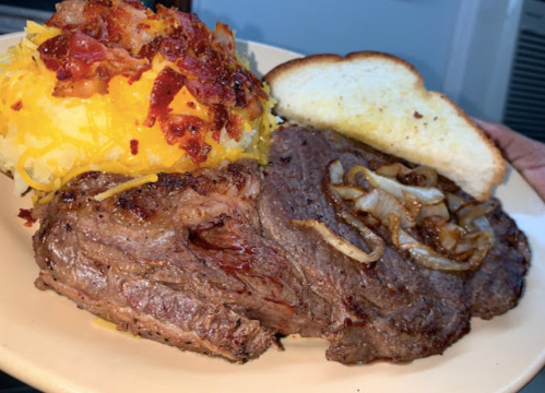 A plate featuring a juicy steak with sautéed onions, a side of cheesy spaghetti squash topped with bacon, and a slice of bread.
