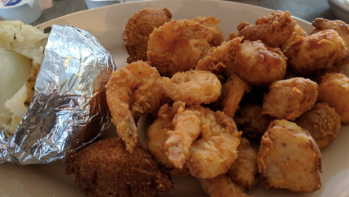 A plate of fried shrimp, hushpuppies, and a baked potato wrapped in foil.