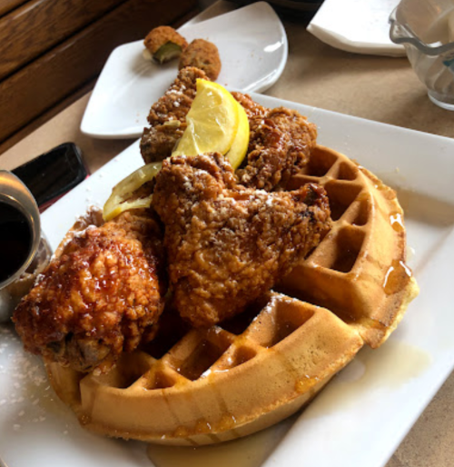 A plate of golden waffles topped with crispy fried chicken and lemon slices, served with a side of syrup.