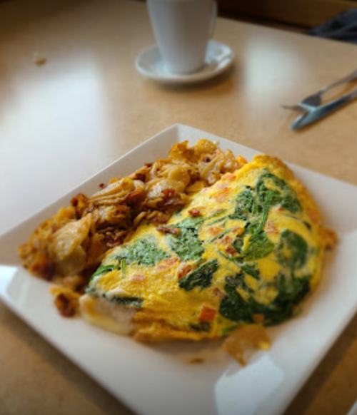 A plate with a spinach omelette and crispy hash browns, with a coffee cup in the background.
