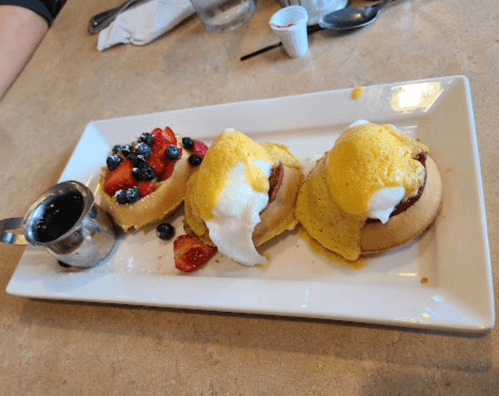 A plate with three servings of pancakes topped with eggs and a side of mixed berries and syrup.