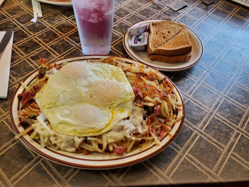 A plate of hash browns topped with two fried eggs and gravy, served with a side of toast and a drink.