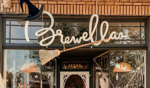 A storefront with the sign "Brewellas," featuring a broom and a witch's hat above the entrance.