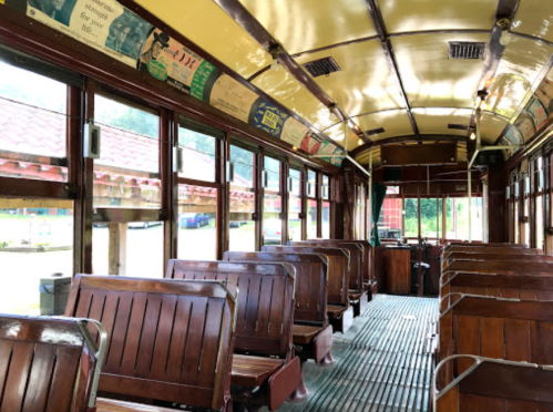 Interior of a vintage tram with wooden benches and a yellow ceiling, featuring large windows and a classic design.