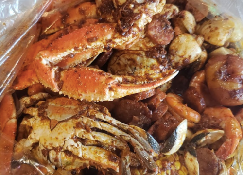 A close-up of a seafood boil featuring crabs, shrimp, sausage, and potatoes, all seasoned and mixed together.
