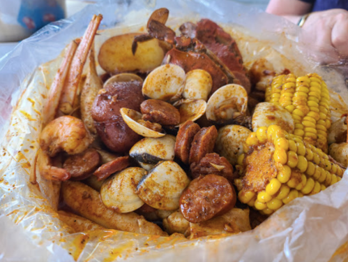 A seafood boil featuring shrimp, crab, clams, sausage, potatoes, and corn, all seasoned and served in a plastic bag.