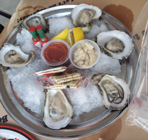 A platter of fresh oysters on ice, accompanied by lemon wedges, cocktail sauce, and condiments.
