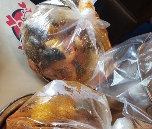 Two large, sealed plastic bags containing dark, possibly cooked food items, resting on a table.