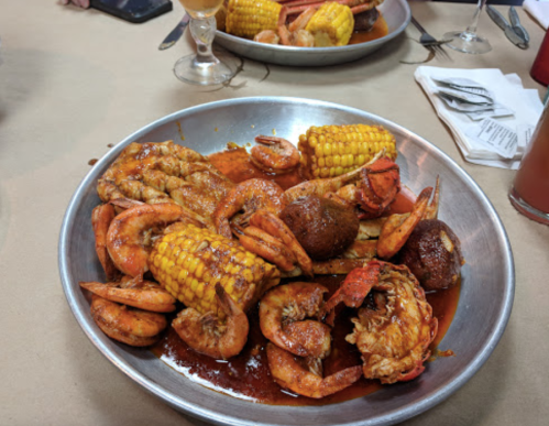 A metal platter filled with shrimp, corn, and crab, all coated in a spicy sauce.
