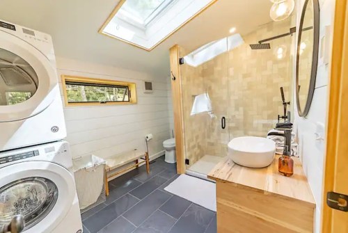 Bright bathroom featuring a shower, modern sink, washer/dryer, and natural light from a skylight.