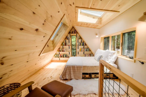 Cozy wooden interior of a triangular-shaped room with a bed, bookshelves, and natural light from skylights.