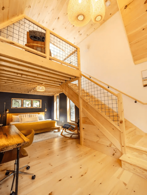 Cozy interior of a wooden cabin featuring a loft, staircase, and modern furnishings in warm tones.