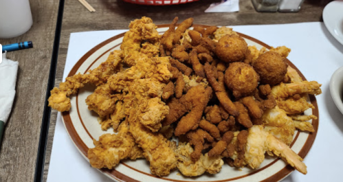 A large plate of fried chicken, hushpuppies, and crispy fried strips, served on a wooden table.