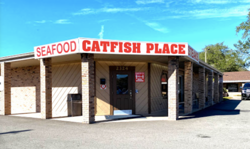 Exterior of a seafood restaurant named "Catfish Place," featuring a brick facade and a clear blue sky.